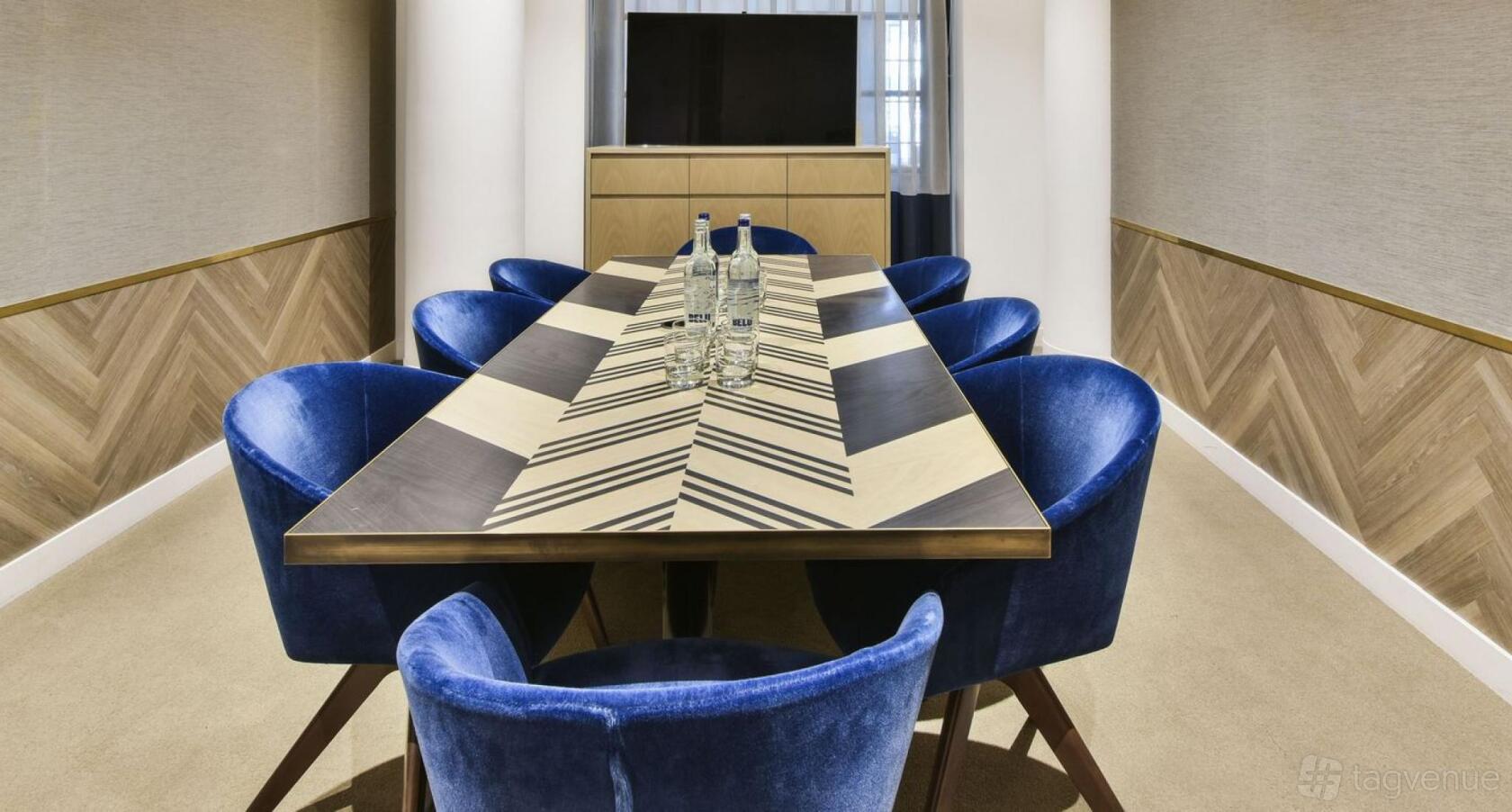 A meeting room with a geometric-patterned table, blue velvet chairs, and bottled water at Michelin House.