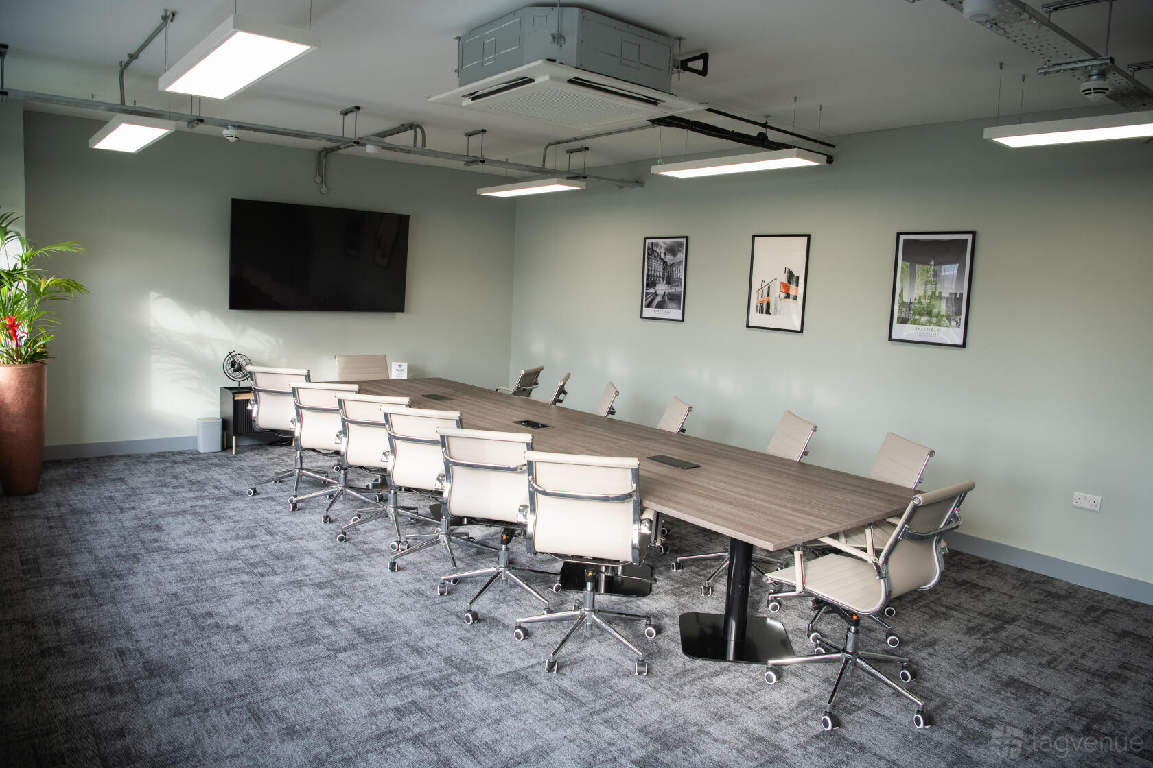 A meeting room with a long conference table, ergonomic chairs, wall-mounted TV, and framed art at Wizu Workspace - Sheffield - Eyre Street.