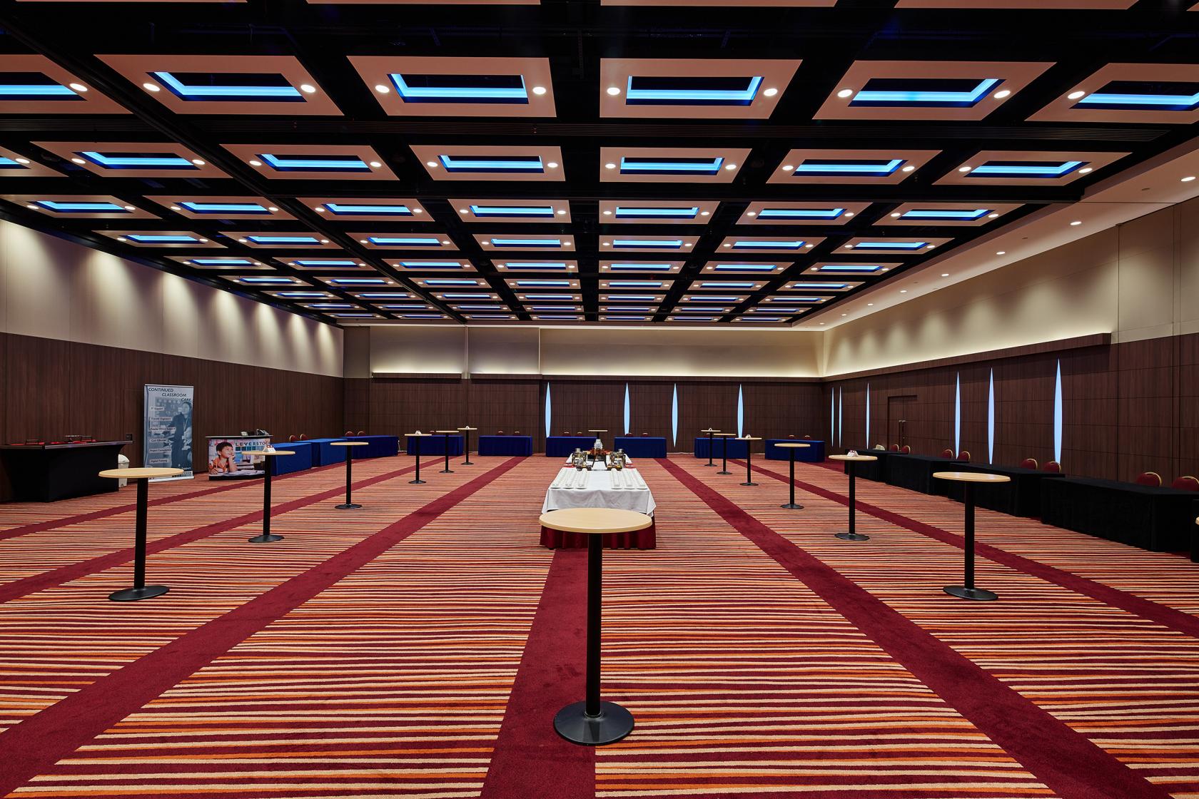 An event space with geometric ceiling lights, striped carpeting, and spaced-out tables at Mercure London Earl's Court.