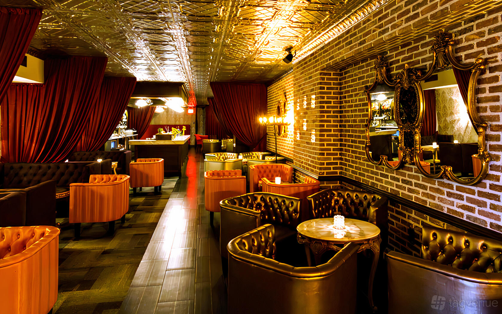A cocktail bar with tufted leather seating, round marble tables, ornate mirrors, and exposed brick walls at The Last Word.