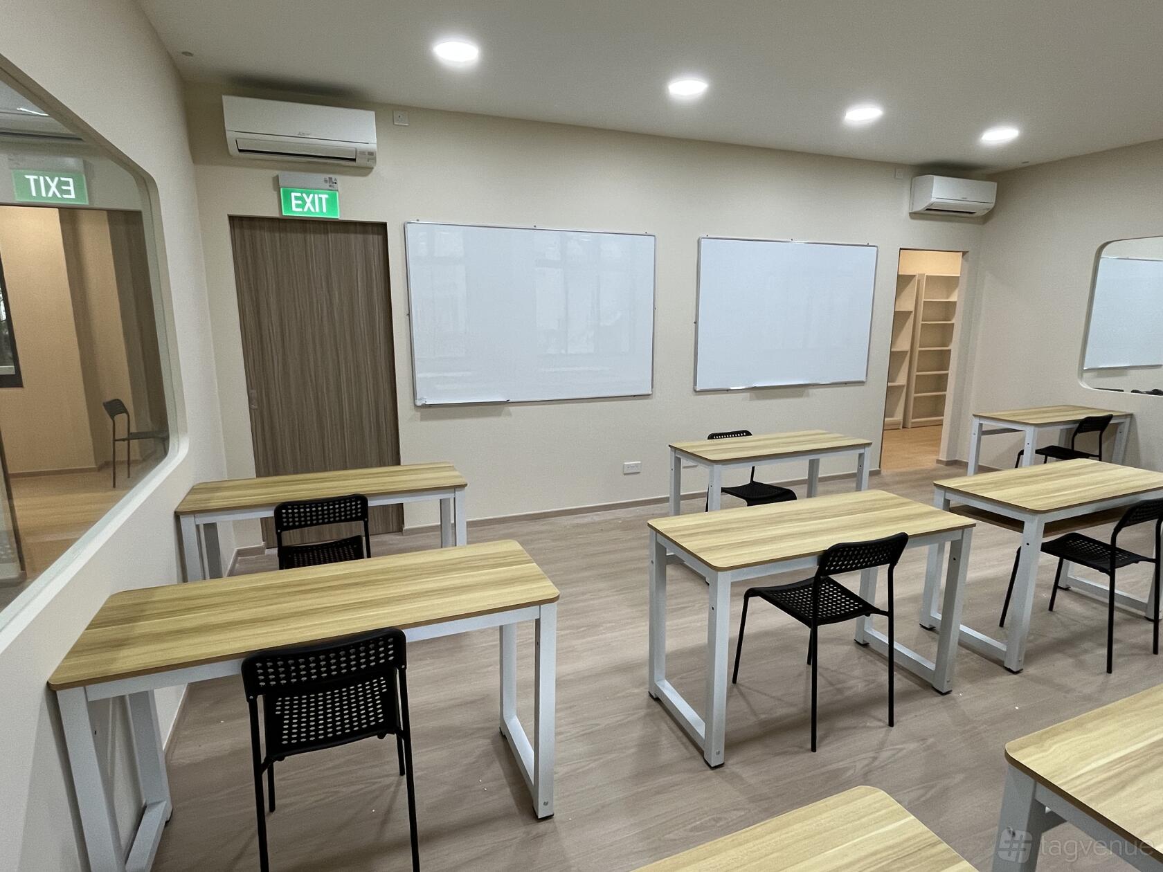 A classroom with wooden desks, black chairs, large whiteboards, and bright overhead lighting at Sages Academy Admiralty.
