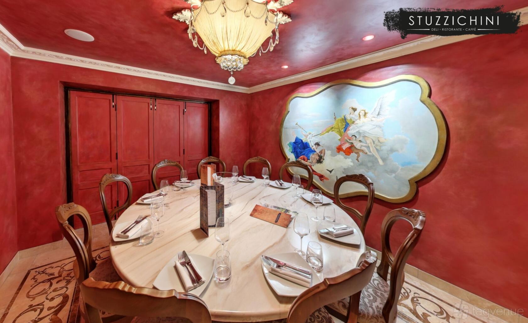 A dining room with a large round marble table, ornate chandelier, and mural of cherubs at Stuzzichini.