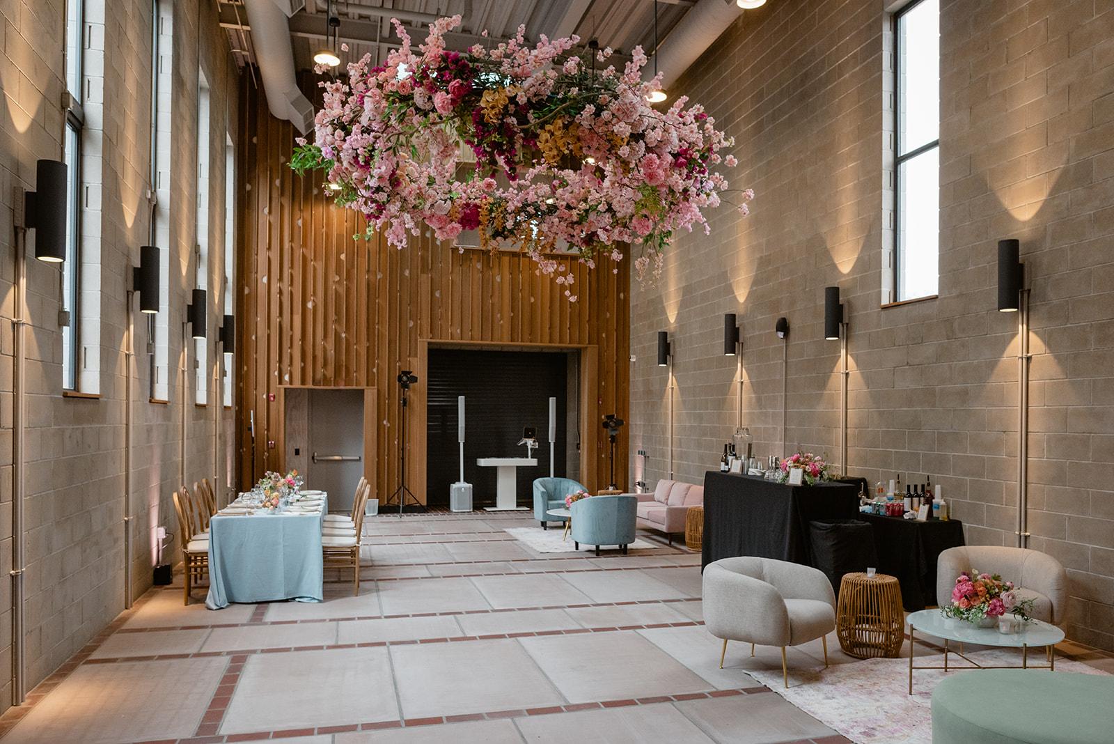 A hall with high ceilings, exposed brick walls, large windows, and a floral installation at Carroll Hall.
