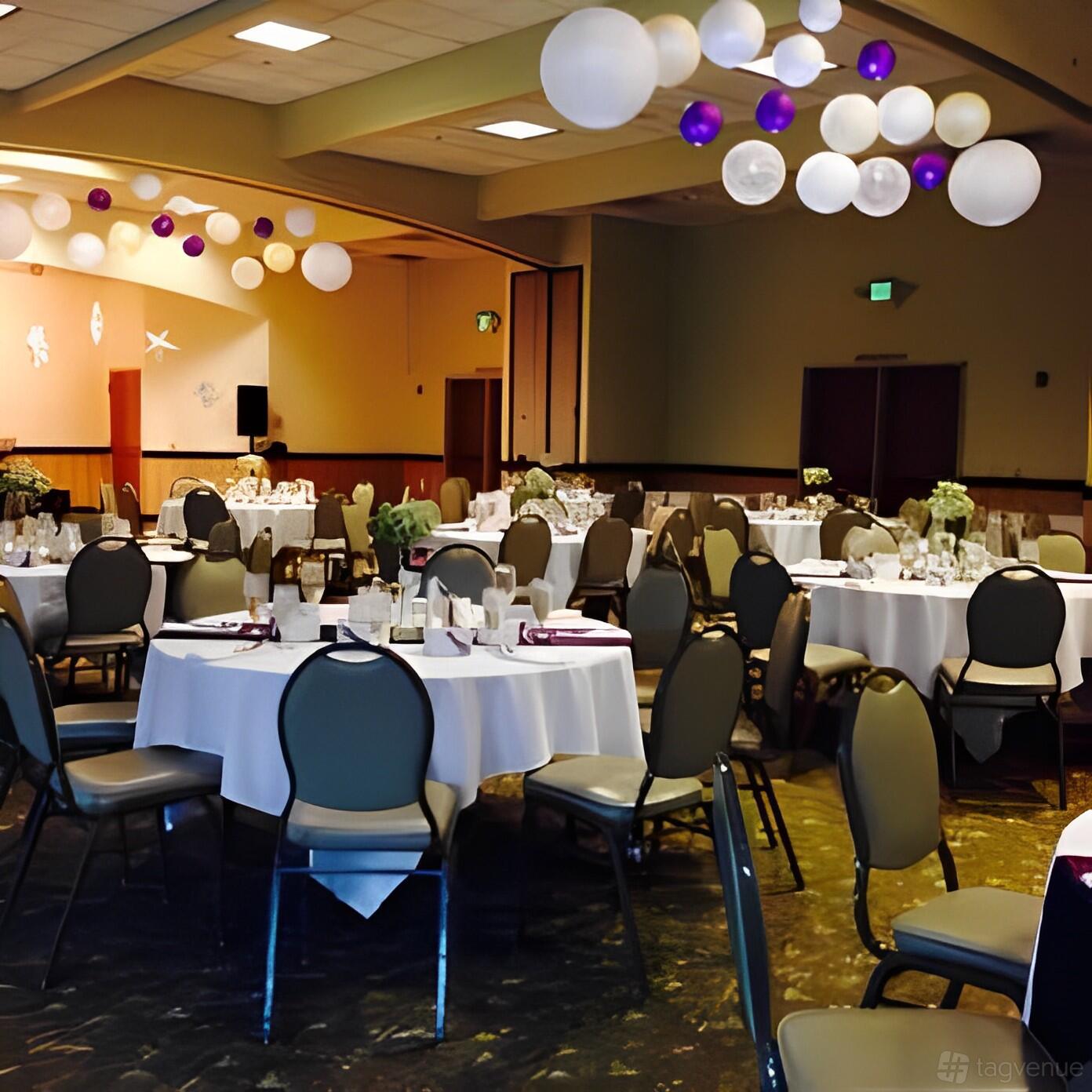 An event venue with round tables, white linens, and balloon decorations at Maplewood Greens.