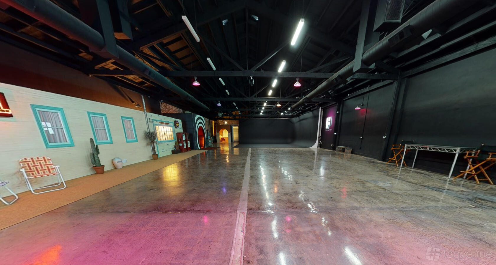 A spacious photo studio with polished concrete floors, blacked-out ceilings, and colorful set facades at Flat Factory Studio.