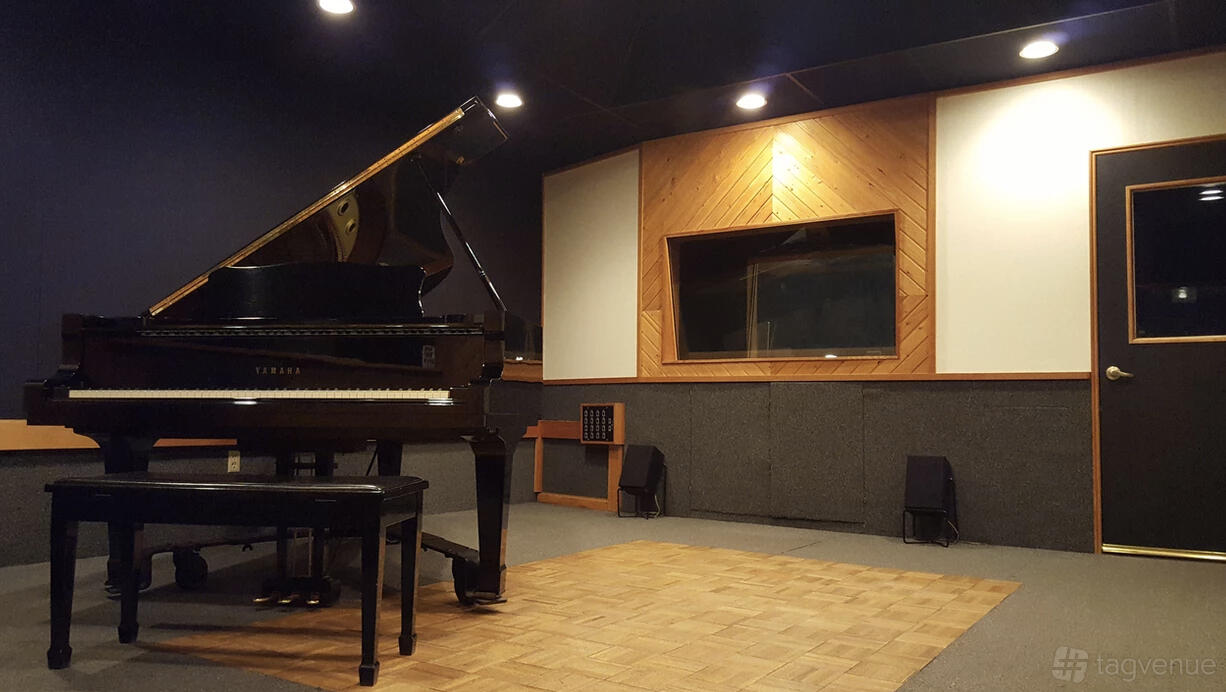 A recording studio with a grand piano, soundproofed walls, and wood acoustic panels at Big City Recording Studios.