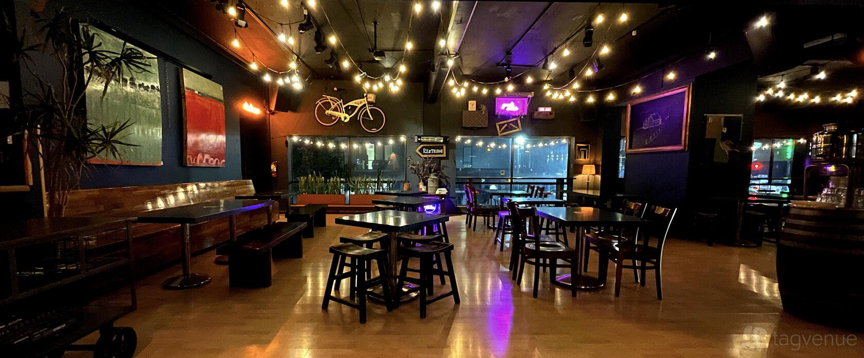 An event space in a bar with string lights, wooden tables, leather banquette seating, and wall art at Upcider.