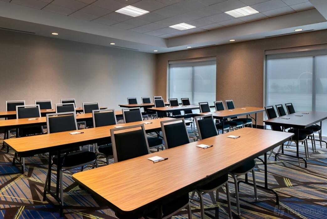 A meeting room with long wood tables, black chairs, notepads, and large windows at Holiday Inn Express & Suites Romeoville.