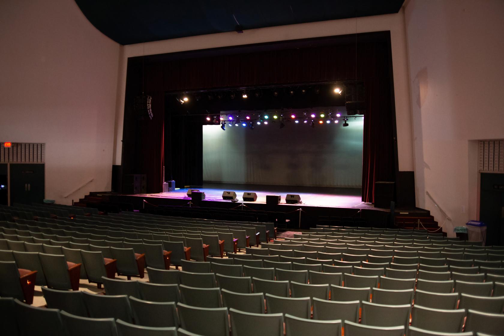 A theatre auditorium with rows of cushioned seats facing a stage with overhead lighting at Oxnard Performing Arts Center Corporation.