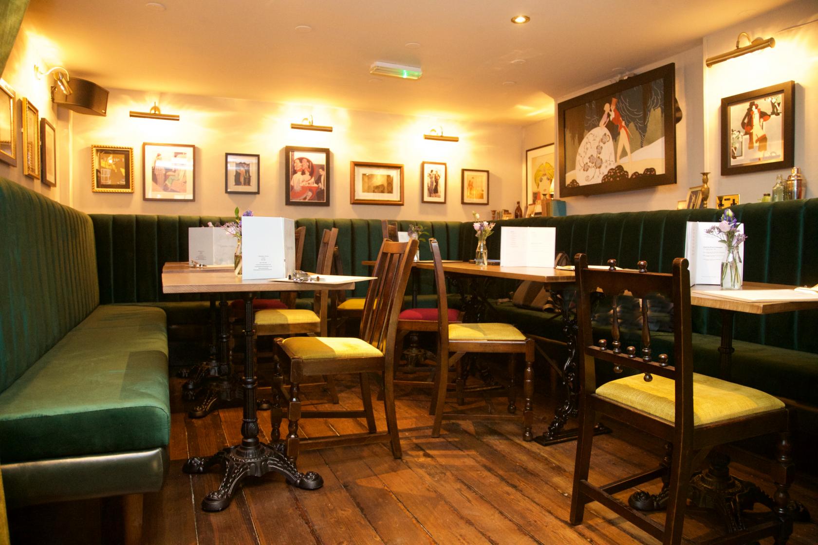 A lounge with green velvet banquette seating, wooden floors, and framed art on the walls at The Champion.