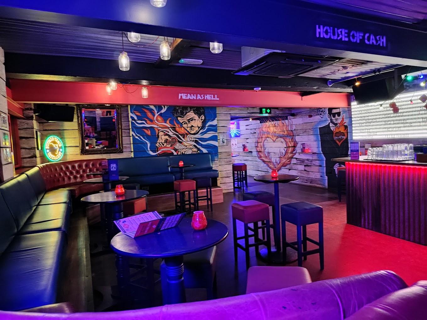 An event space in a bar with neon signs, graffiti art, round tables, and red leather booths at Mean Eyed Cat Liverpool.