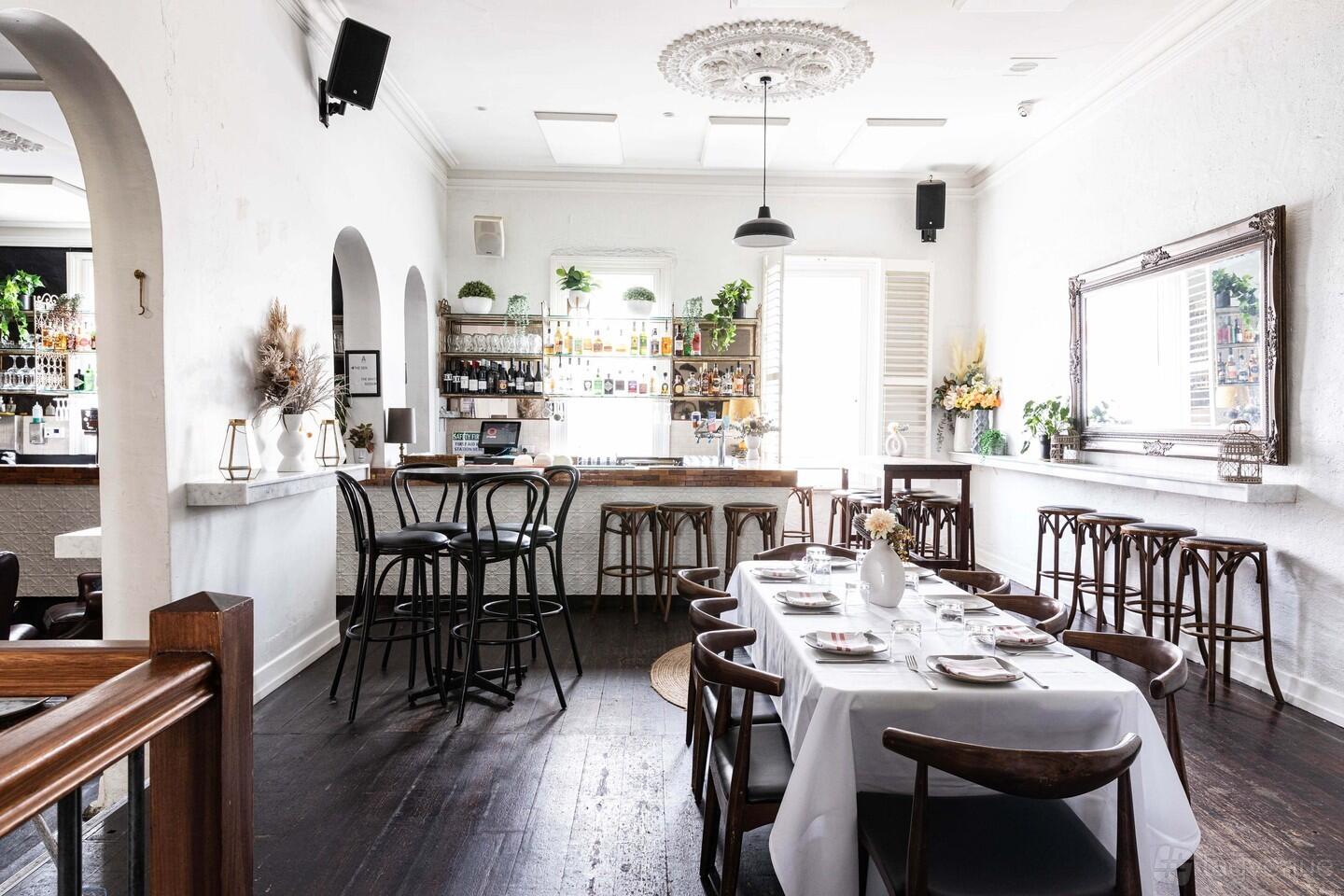 A function room with dark wood floors, a long dining table set with white linens, and a mirrored bar at Aviary Hotel.