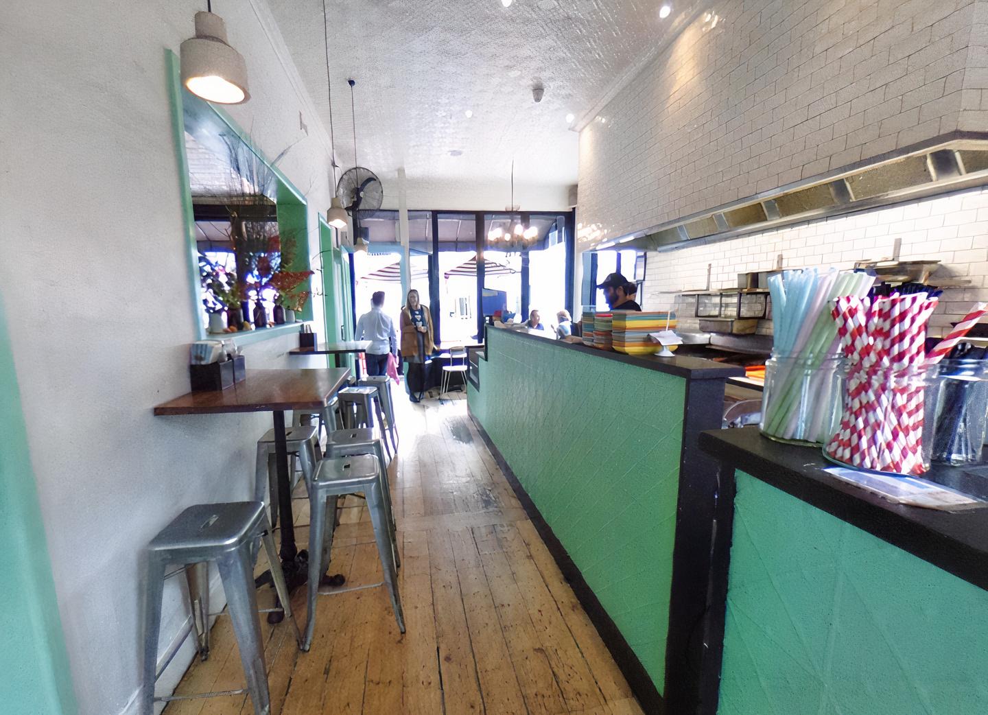 A restaurant with wooden floors, high metal stools, mint green accents, and white tiled walls at Fonda Mexican @ Richmond.