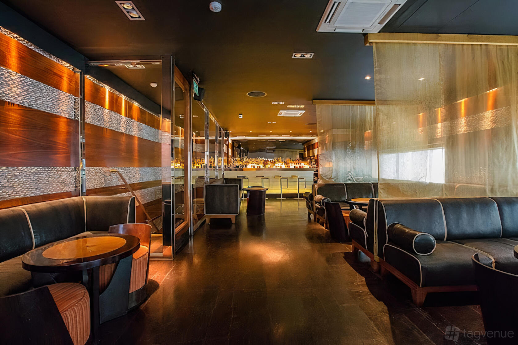 An event space in a restaurant with black leather sofas, wooden tables, and a backlit bar at Mint Leaf Lounge & Restaurant.