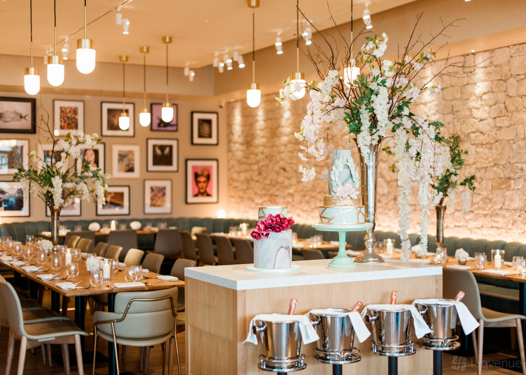 A restaurant with exposed stone walls, framed artwork, banquet seating, and floral centerpieces at Fiume.