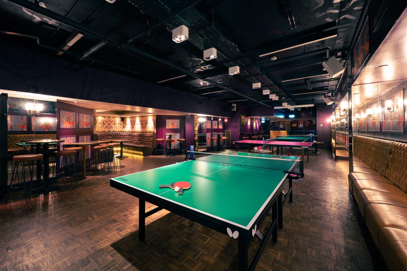 A function room in a bar with table tennis tables, parquet flooring, and plush booth seating at Bounce Farringdon.