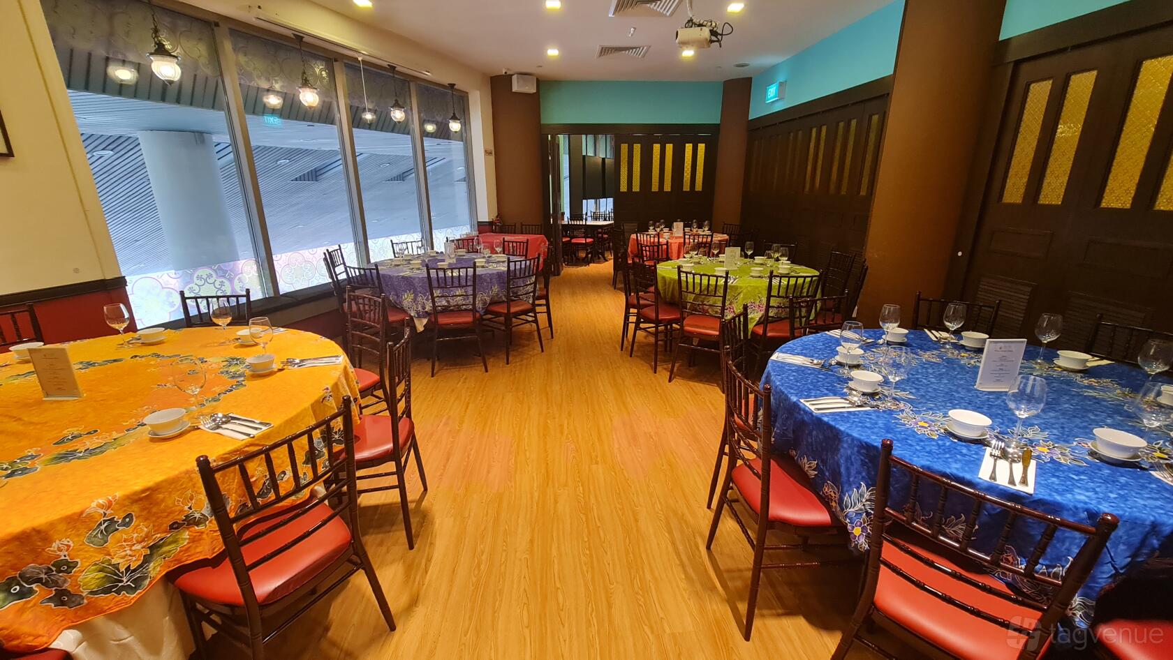 A restaurant with floor-to-ceiling windows, wood flooring, and colorful round tables at Straits Chinese Nonya Restaurant - Raffles.