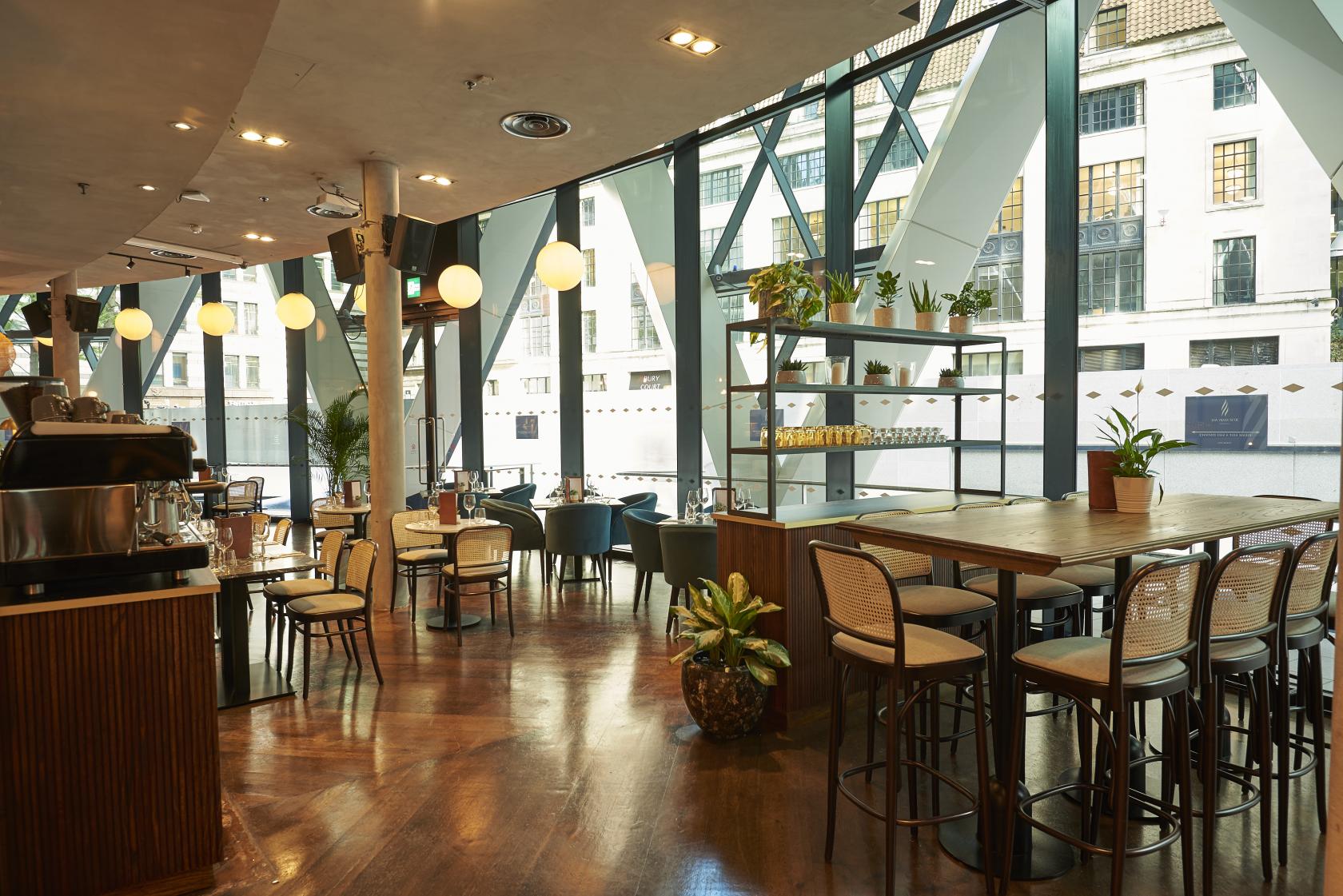 A restaurant with floor-to-ceiling windows, wood floors, globe pendant lights, and a mix of tables at The Sterling.