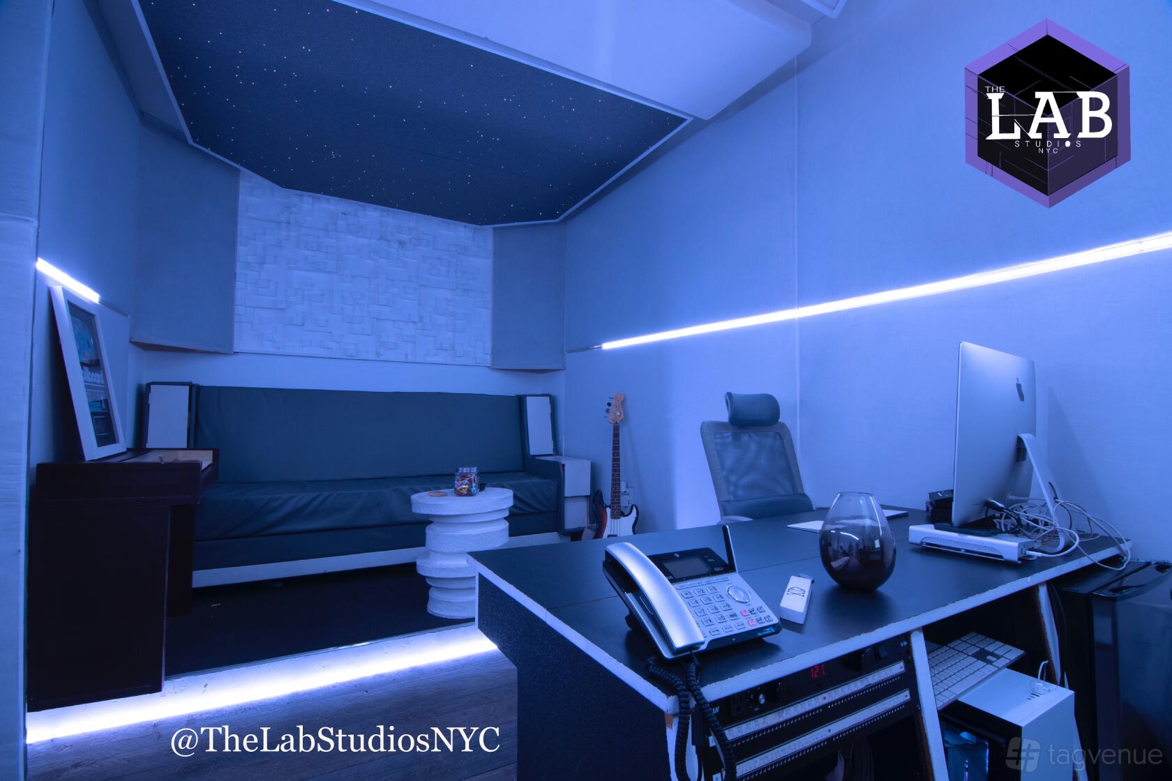 A recording studio with blue LED lighting, acoustic wall panels, a sofa, and a desk with studio equipment at TheLabStudiosNYC.