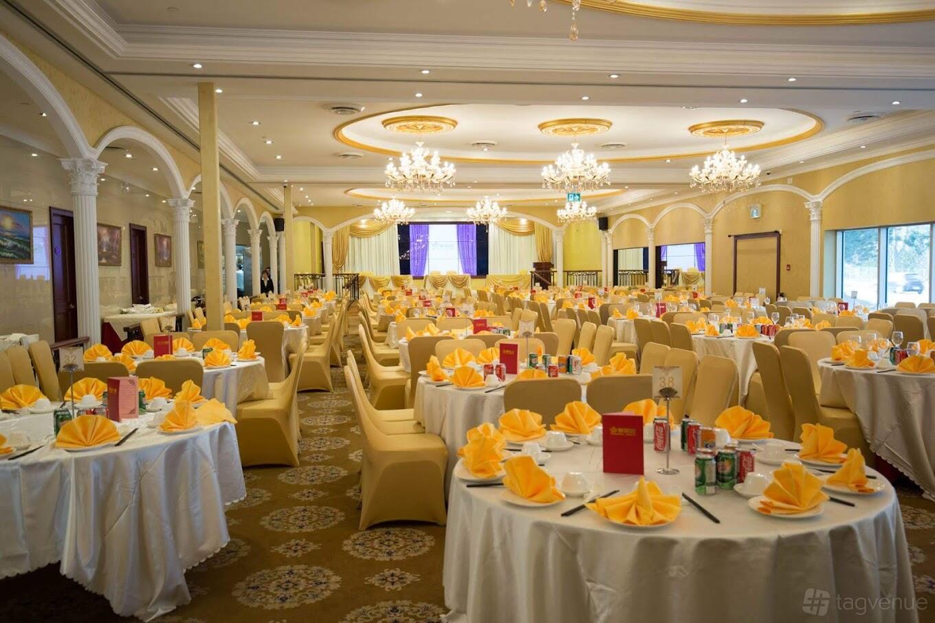 A banquet hall with round tables set with folded yellow napkins, chandeliers, and gold accents at Grandeur Palace.