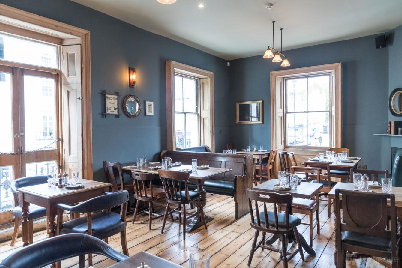A pub dining room with wooden floors, large windows, and wooden tables with mismatched chairs at Marquis of Westminster.