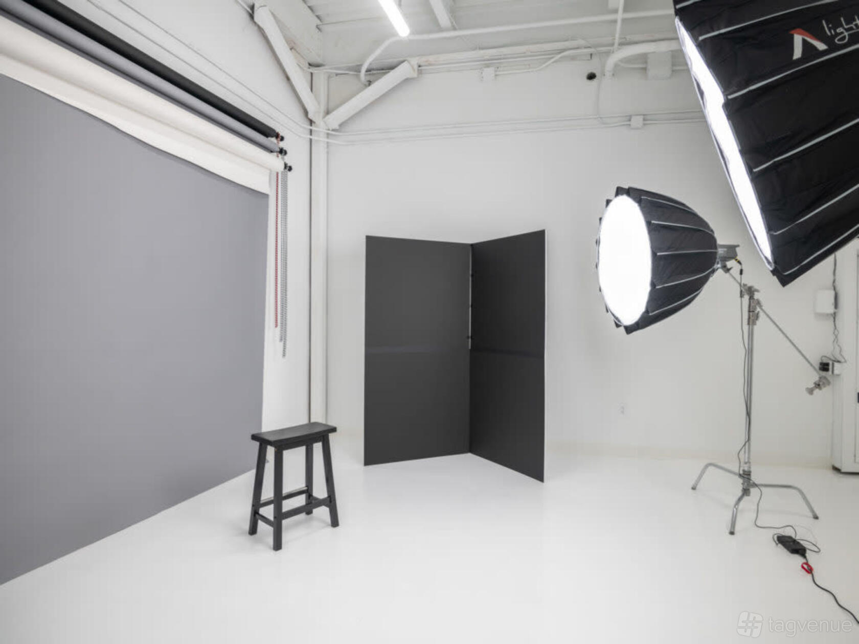 A photo studio with a gray backdrop, black stool, and professional lighting equipment at Light Box Dallas.