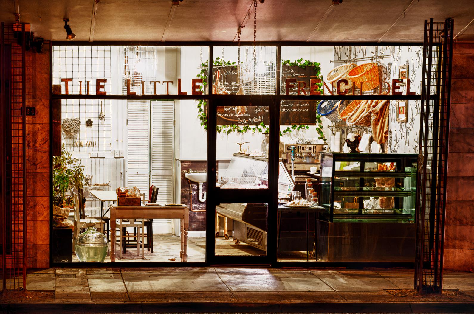 A restaurant with large street-facing windows, a display counter, and hanging bread at The Little French Deli & Bistro.