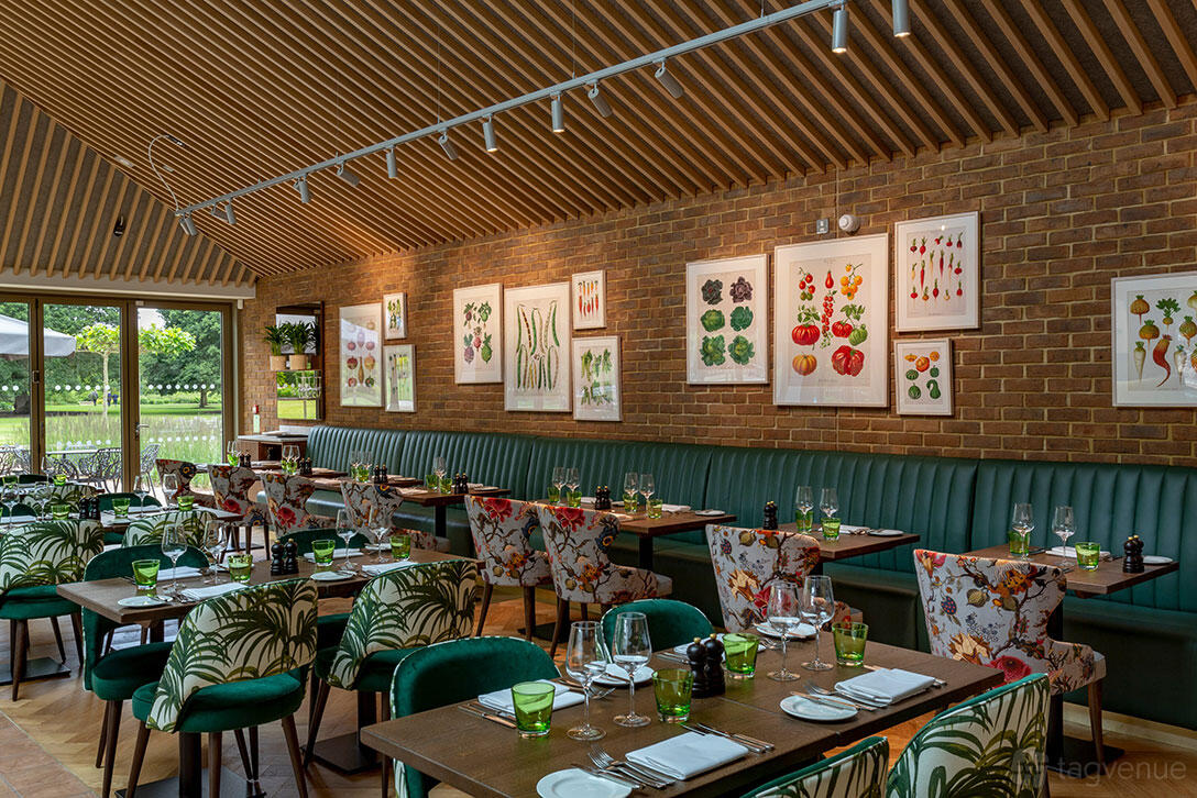A restaurant with botanical artwork, green upholstered seating, and floor-to-ceiling windows at RHS Garden Wisley.