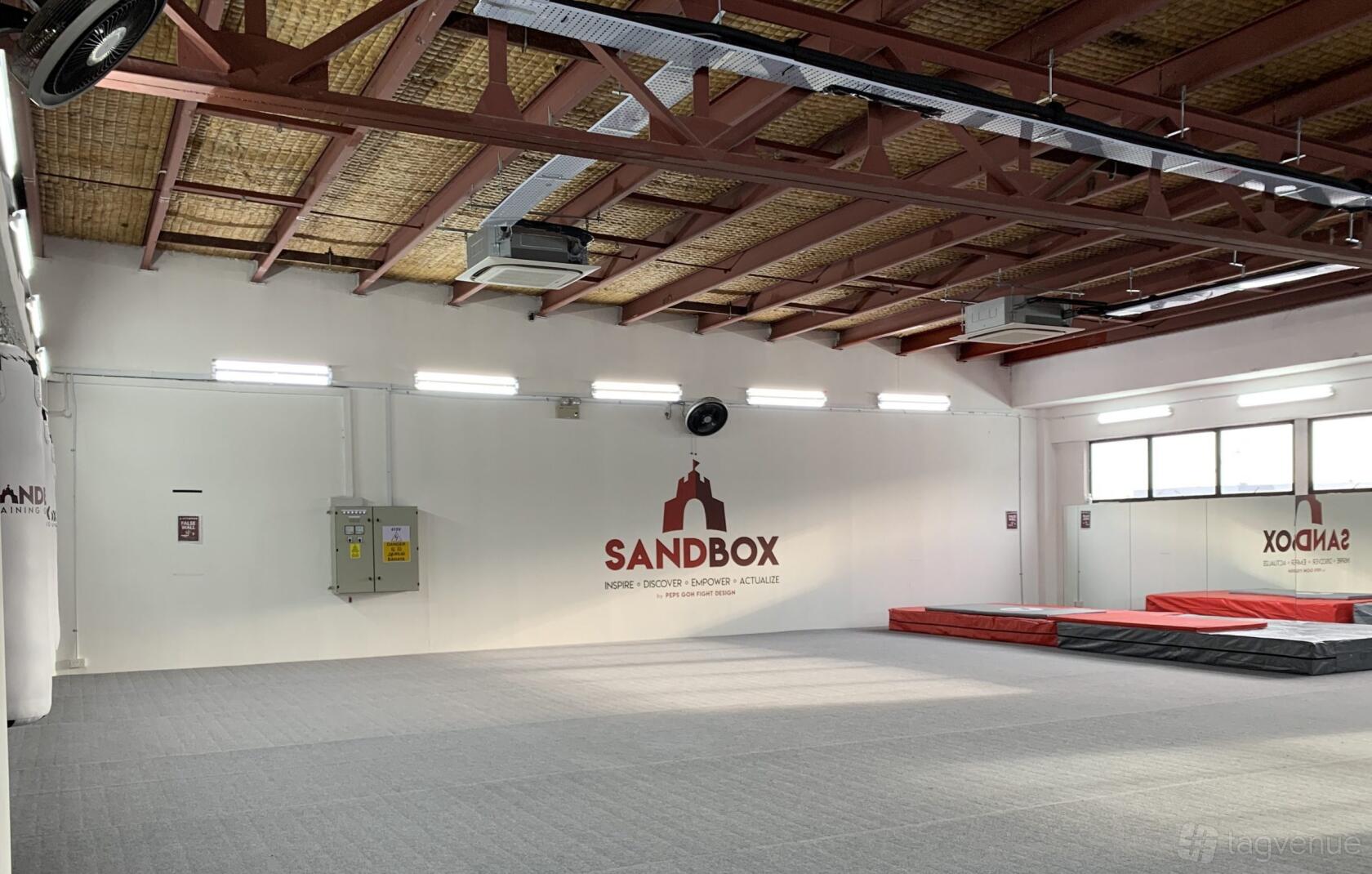 A fitness studio with padded flooring, exposed beams, and wall mats at Sandbox Training Ground.