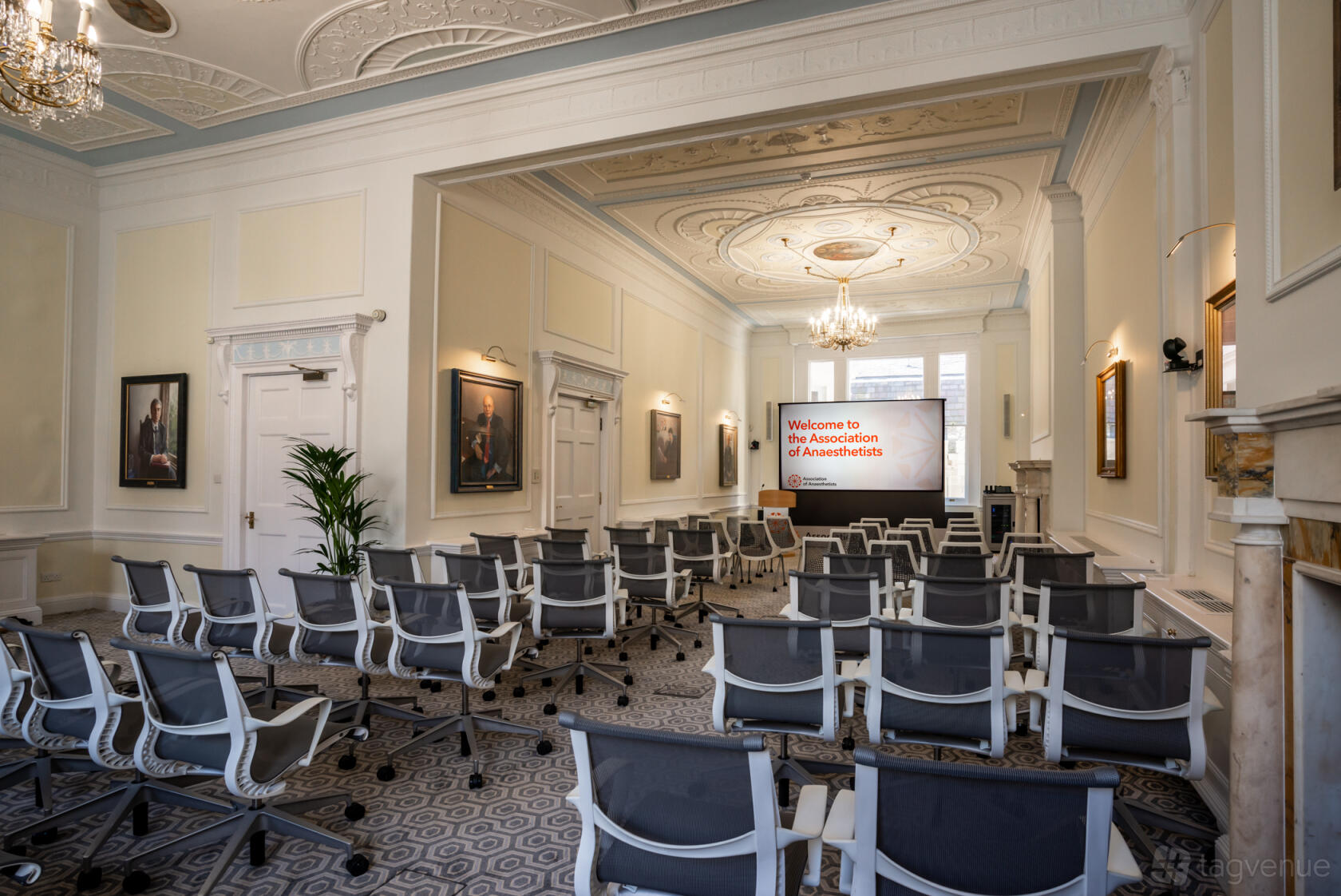 An event venue with rows of modern chairs, chandeliers, and a decorative ceiling at 21 Portland Place.