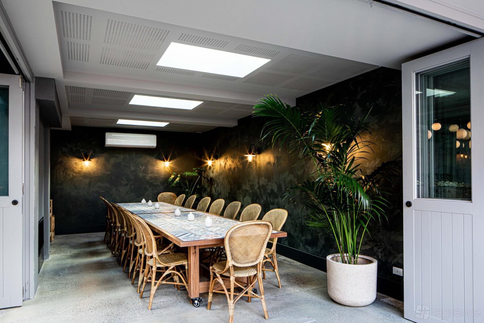 A private dining room in a bar with a long wooden table, woven chairs, and skylights at Teller.