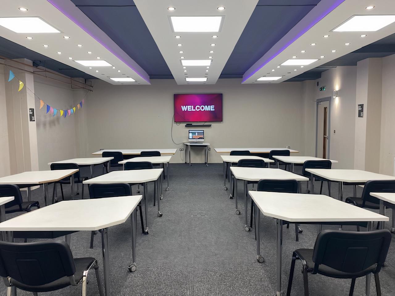 A meeting room with rectangular tables, black chairs, carpeted floor, and a wall-mounted screen at Destiny Church City.