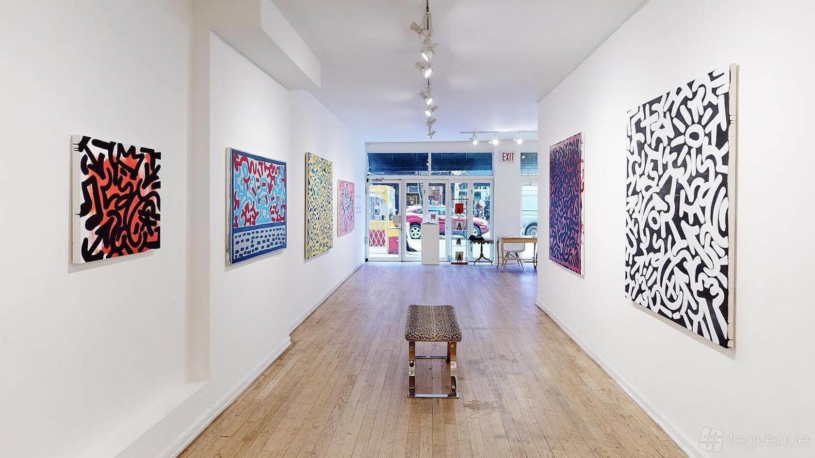 A gallery with white walls, wooden floors, colorful abstract art, and track lighting at Van Der Plas Gallery.