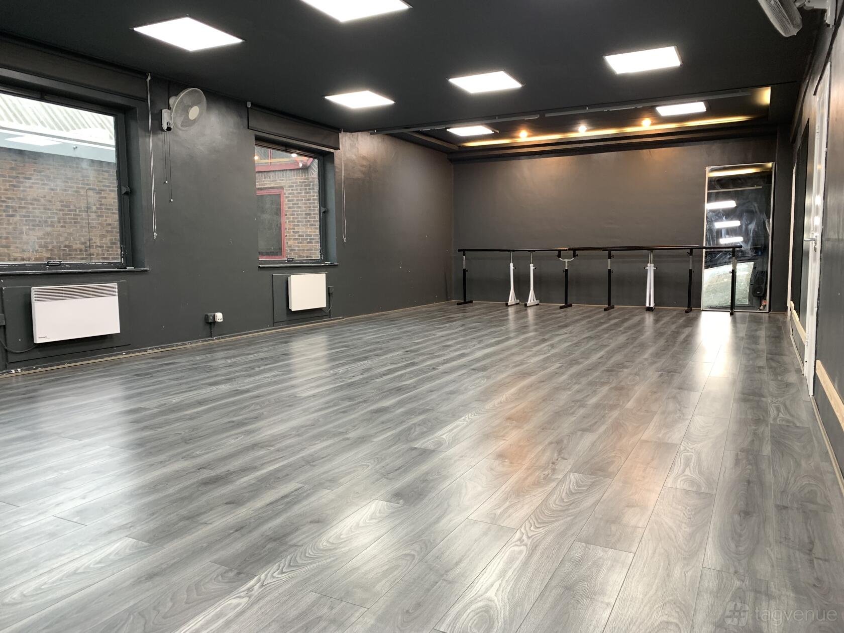 A dance studio with gray wood floors, wall-mounted barres, and large windows at ECD - EUROPEAN COLLEGE OF DANCE.