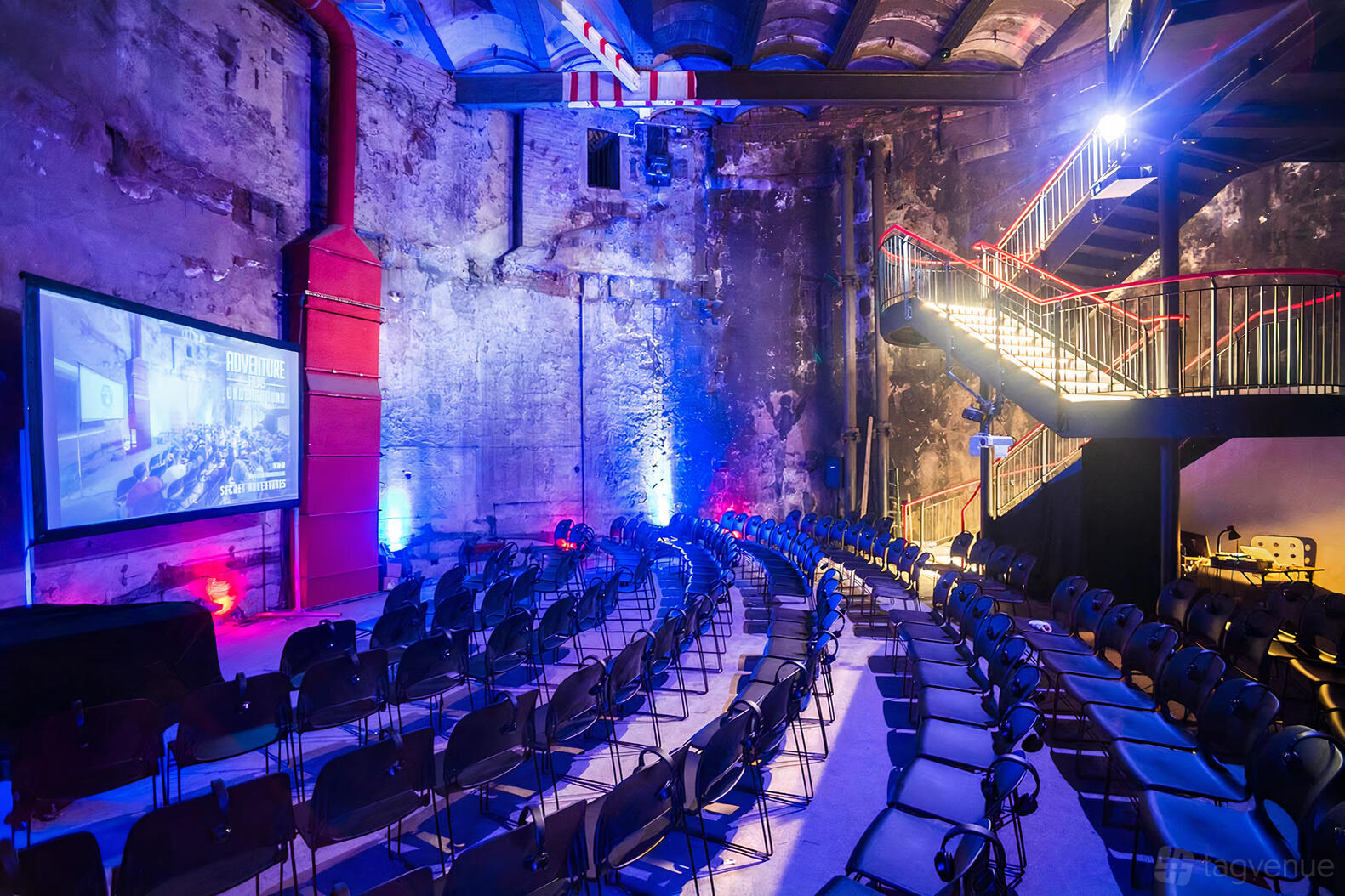 An event space in a museum with exposed brick walls, rows of chairs, and a projection screen at The Brunel Museum.