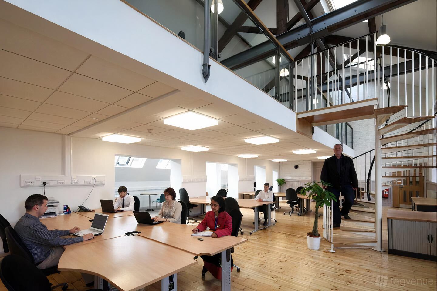 An office workspace with wooden floors, open desks, natural light, and a spiral staircase at Heart Centre.