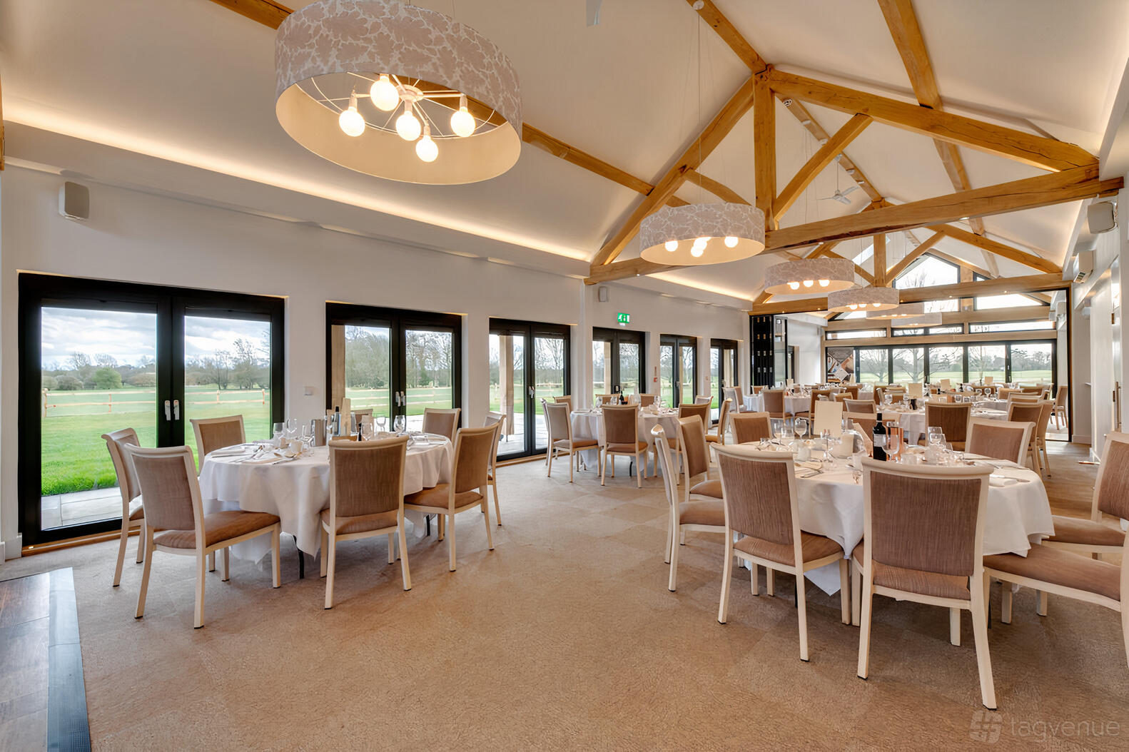 A country house event room with exposed wooden beams, round tables set for dining, and large windows at Fynn Valley Terrace.