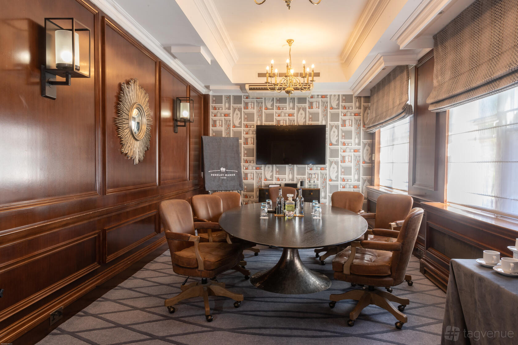A hotel meeting room with a round table, leather swivel chairs, wood-paneled walls, and large windows at Pendley Manor Hotel.
