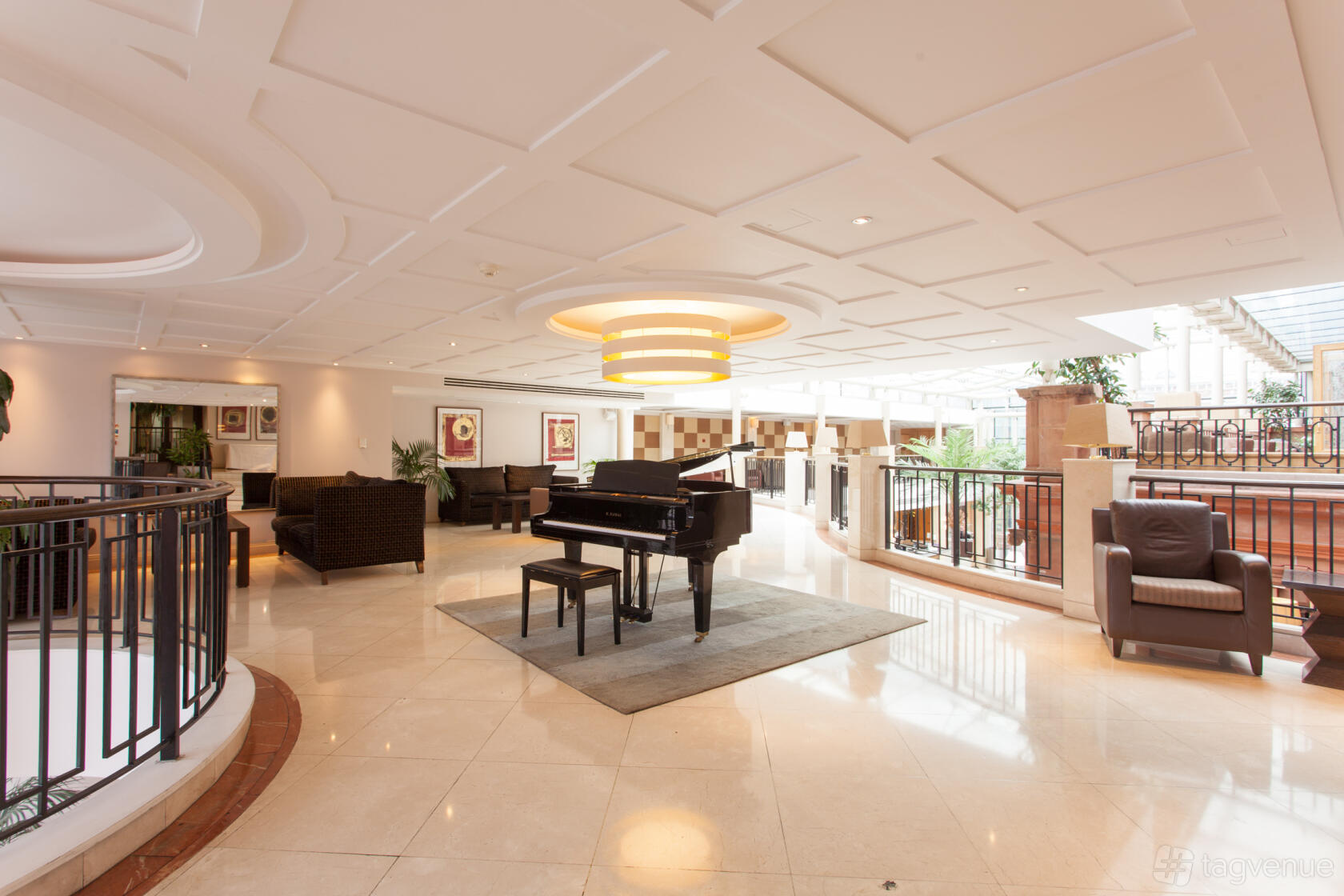 A hotel lounge with a grand piano, armchairs, and sofas beneath a large ceiling light at The Crown London Hotel.