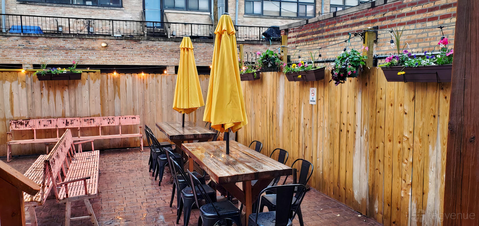 An outdoor bar space with wooden tables, yellow umbrellas, brick flooring, and planters at Gold Star Bar.