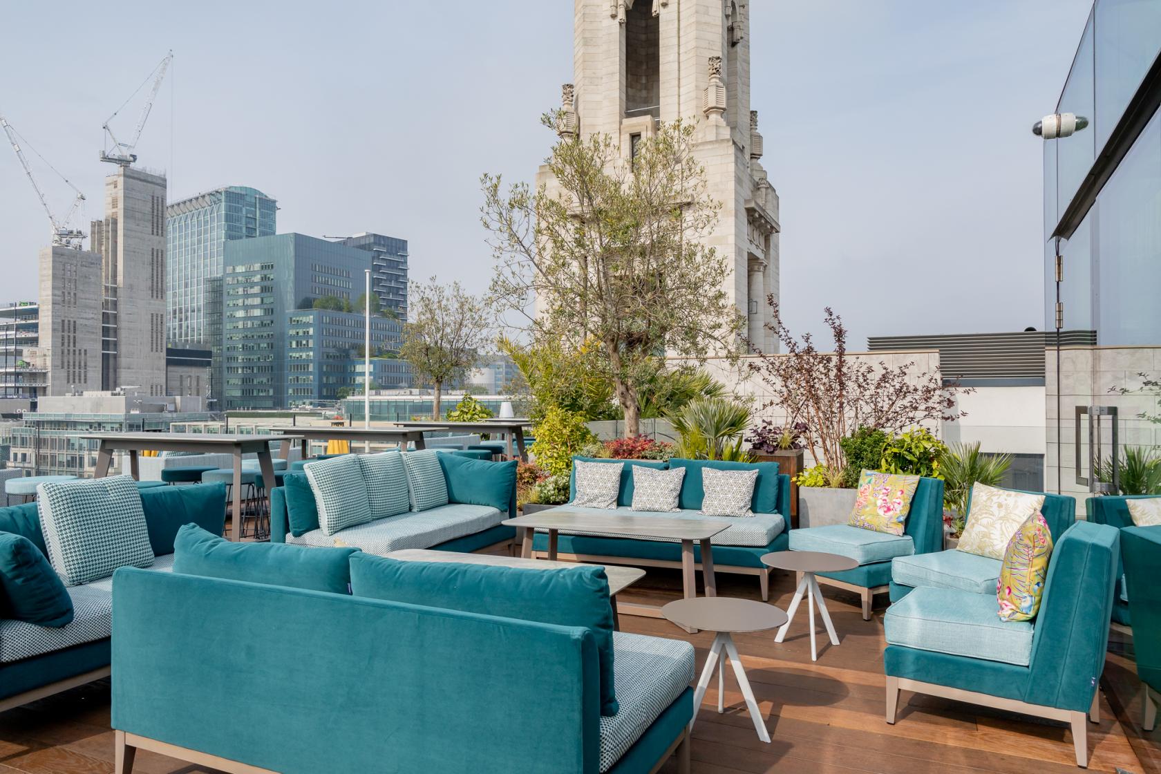 A rooftop lounge with teal cushioned seating, low tables, and cityscape views at Aviary Rooftop Bar & Restaurant.
