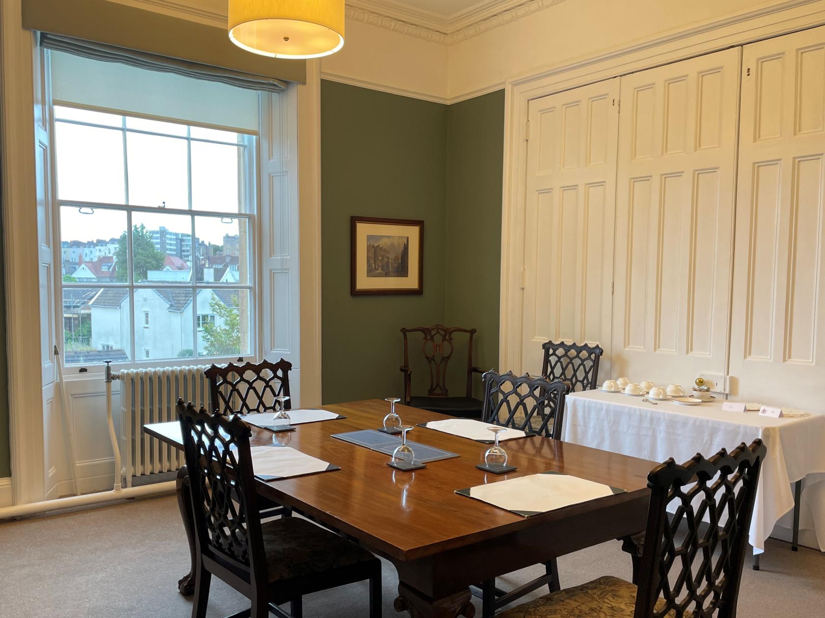 A meeting room with a polished wooden table, lattice-back chairs, and large windows at Merchants' Hall.