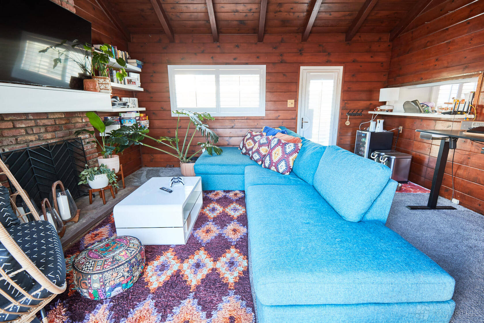 A photo studio with wood-paneled walls, a brick fireplace, blue sectional sofa, and colorful rug at Iroquois.