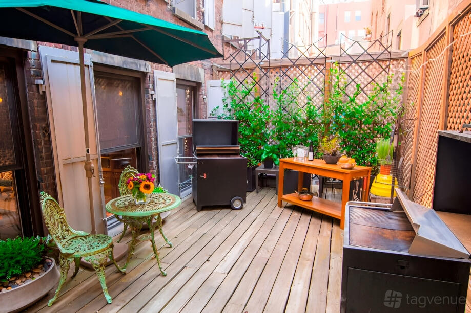 An outdoor event venue with wooden decking, a grill station, green bistro set, and trellis planters at Miette Culinary Studios Inc.