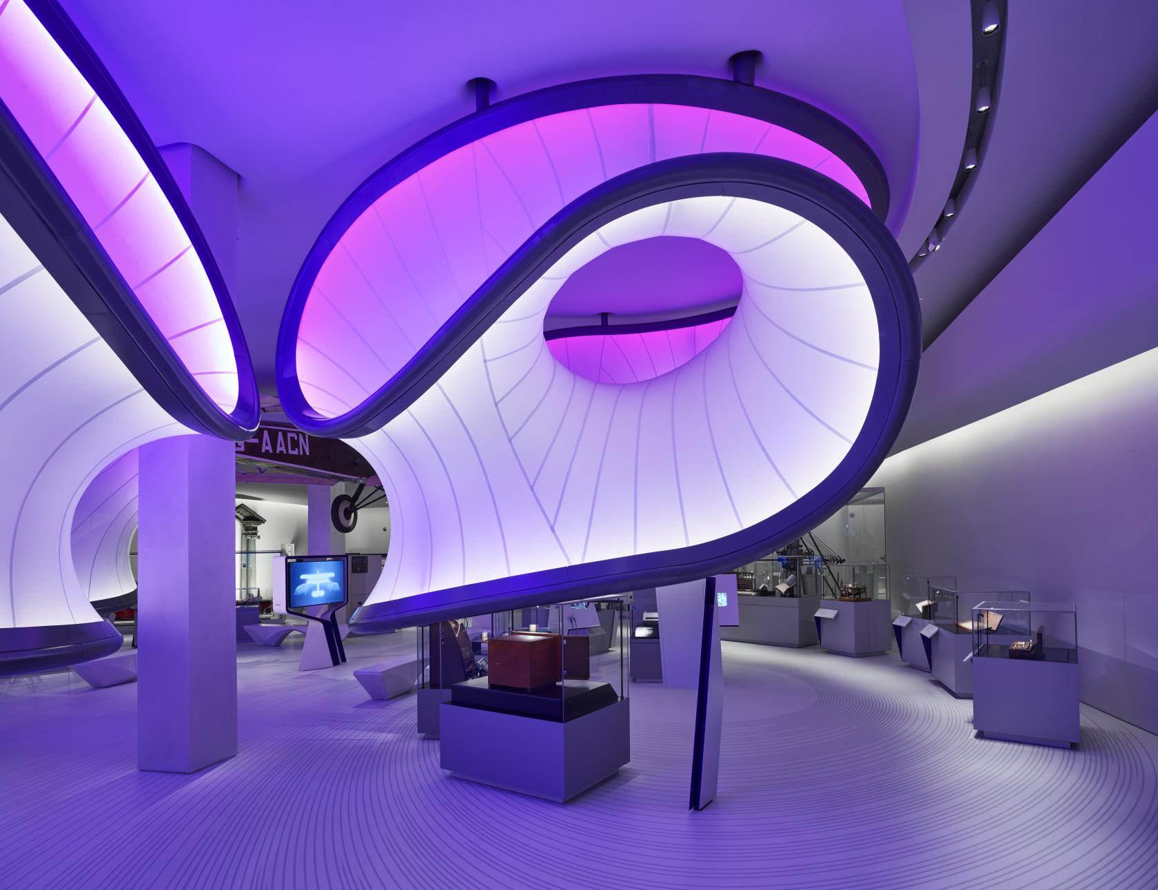 A museum gallery with large illuminated curved installations and glass display cases at Science Museum.