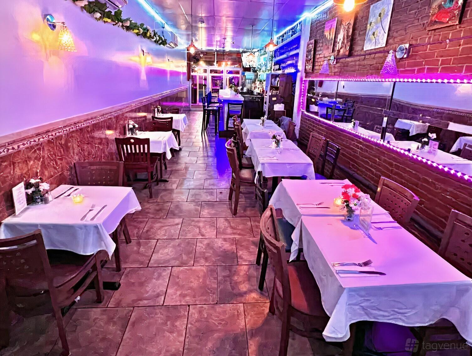 A restaurant with tables draped in white linens, wooden chairs, brick walls, and colorful LED accent lighting at Fusion HK Bar and Grill.