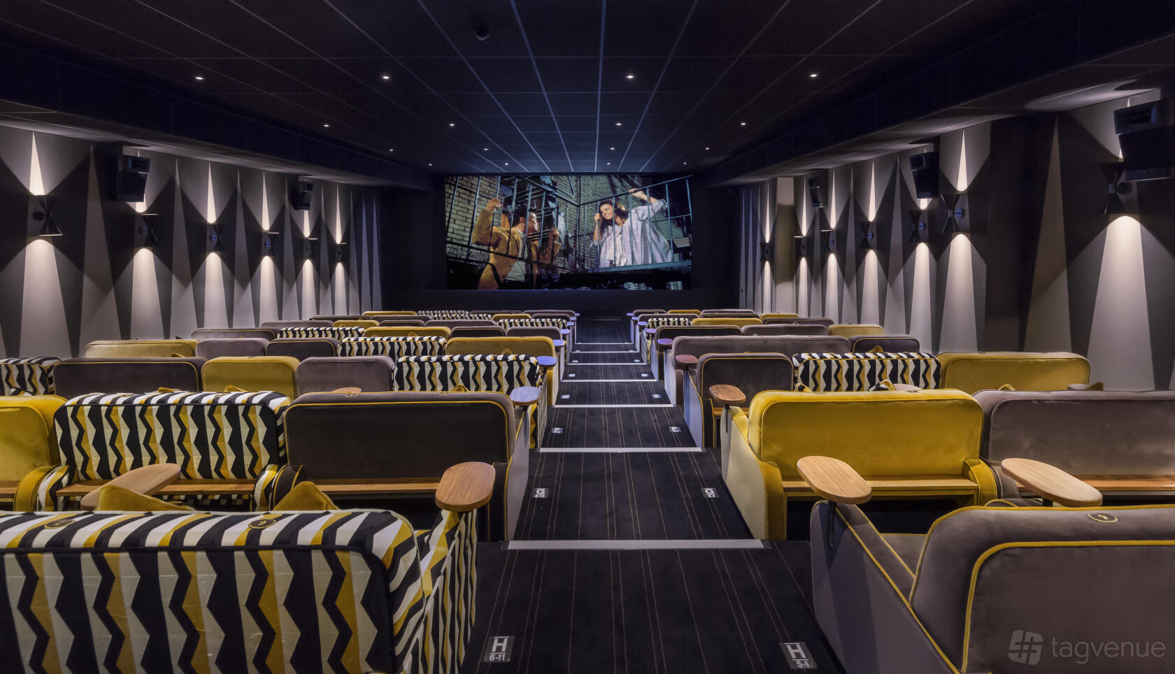 A screening room with patterned and velvet armchairs, aisle lighting, and a large projection screen at Everyman Kings Cross.