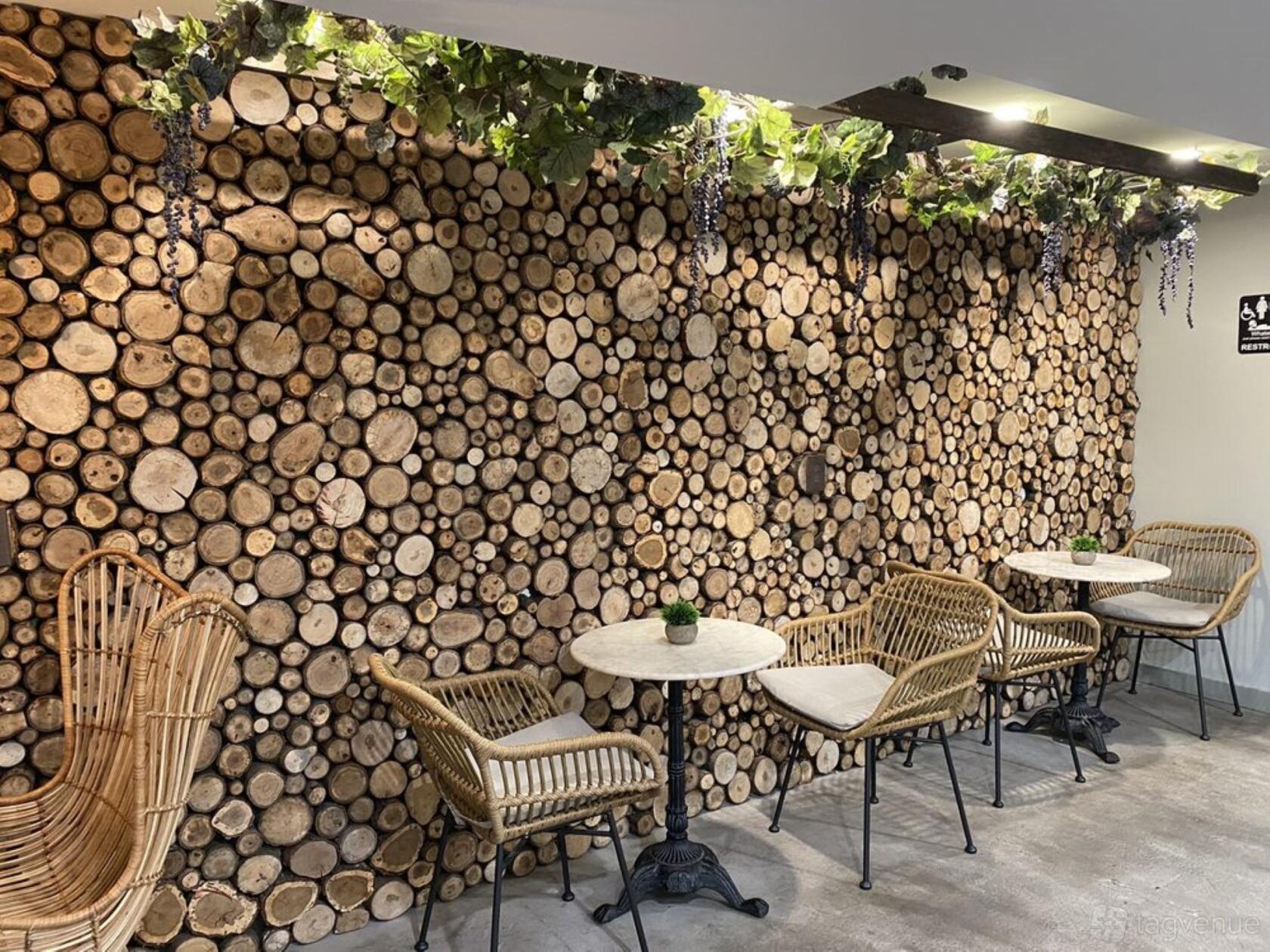 An event space in a restaurant with round marble tables, wicker chairs, and a wood log feature wall at Zeleno.