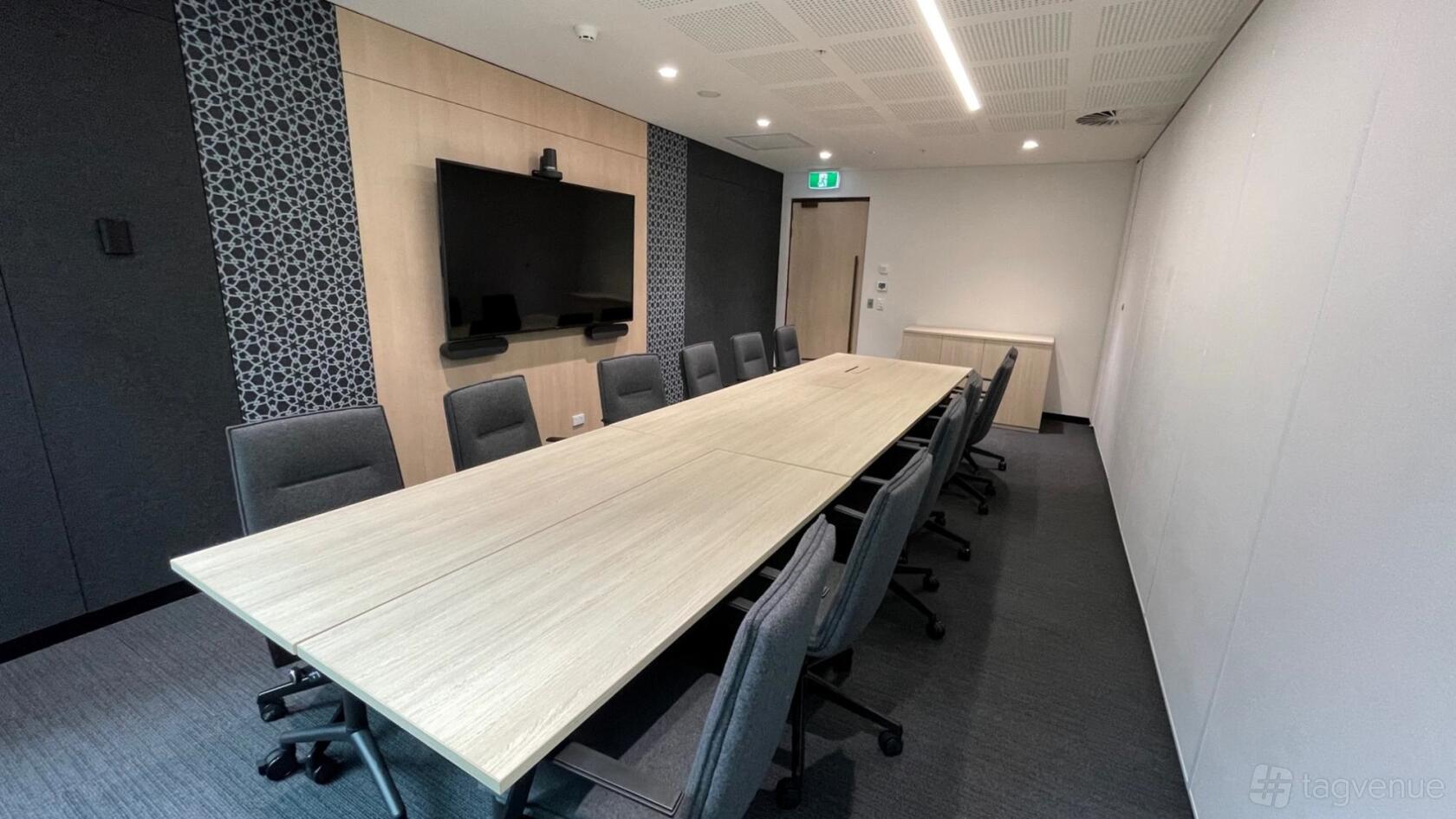 A meeting room with a long wooden conference table, grey chairs, and a wall-mounted screen at 275 George Street.
