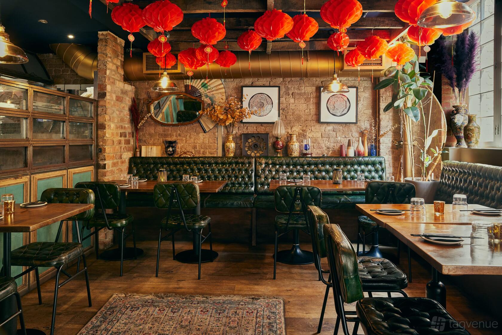 An event space in a restaurant with tufted green banquettes, exposed brick walls, and red lanterns at The Last Talisman.